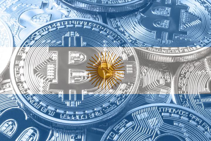A pile of metal coins intended to represent Bitcoin superimposed with an image of the flag of Argentina.